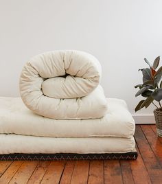 a pile of pillows sitting on top of a wooden floor next to a potted plant