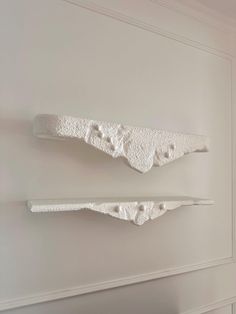 two white sculptures are hanging on the wall