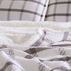 an unmade bed with white and grey plaid blankets on it's sides, next to a pillow