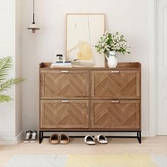 a wooden dresser with shoes on it in front of a plant and pictures hanging on the wall