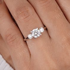 a woman's hand with three stone engagement ring on her left and right hand