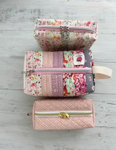 three zippered pouches are stacked on top of each other, one is pink and the other is gray