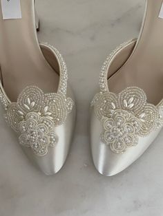 a pair of white wedding shoes with pearls and lace on the heel, sitting on a marble surface