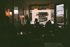 people sitting at tables in front of a coffee shop with cars parked outside the window