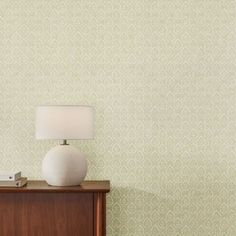 a white lamp sitting on top of a wooden dresser next to a wallpapered wall