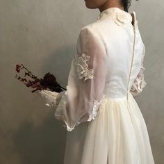 a woman wearing a white dress and holding a bouquet of flowers in front of a wall