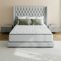 a white bed with two pillows on top of it and a night stand in the background