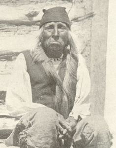 an old black and white photo of a man with long hair sitting on the ground