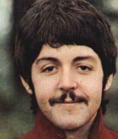 a man with a moustache on his face is smiling at the camera while wearing a red shirt