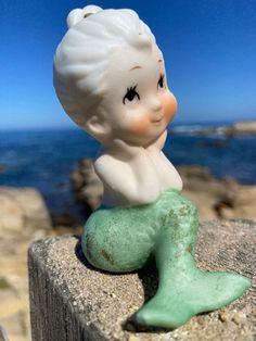 a little figurine sitting on top of a rock next to the ocean