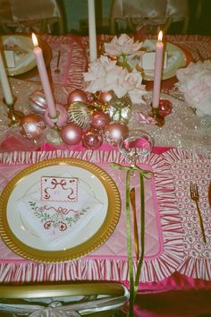 the table is set with pink and gold plates, silverware, candles, and flowers