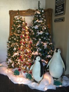 two penguins are standing in front of a christmas tree