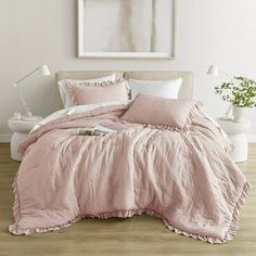 a bed with pink comforter and pillows in a white room next to a painting on the wall