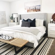 a white bedroom with black and white accessories on the bed, rugs and pillows