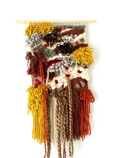 a wall hanging made out of different colored yarns and ropes with pine cones on top