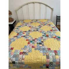 a bed with a yellow quilt on top of it and a white headboard in the background