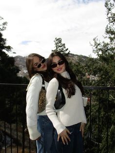 two young women standing next to each other on top of a metal fence with trees in the background