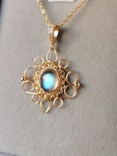 a gold necklace with a blue stone in the center on a gray surface, sitting on top of a white box