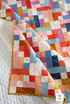 a colorful quilt on top of a bed with white sheets and polka dot trims