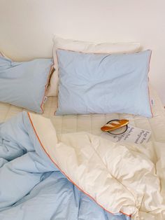 an unmade bed with blue and white sheets, pillows and a book on it