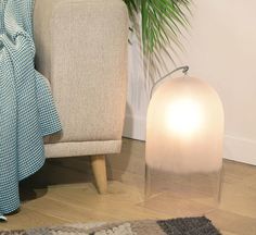 a white lamp sitting on top of a wooden floor next to a chair and potted plant