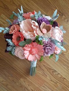 a bridal bouquet with pink, purple and green flowers on the floor in front of a phone