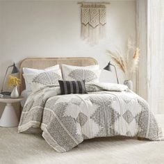 a bed with white and grey comforter in a bedroom next to a lamp on a table