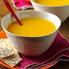 two bowls of carrot soup with crackers on the side