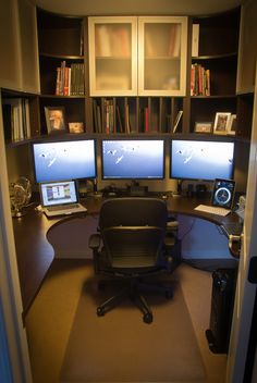 a computer desk with two monitors and a laptop on it in front of bookshelves