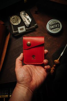 a person holding a red wallet next to some other items