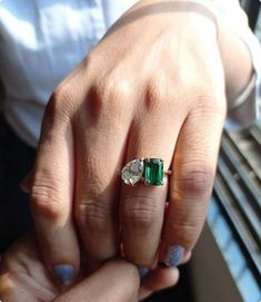 a woman's hand holding an emerald and diamond ring