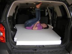 a woman laying on top of a white mattress in the back of a car trunk