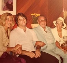 an older man and two younger women sitting next to each other on a couch in a living room