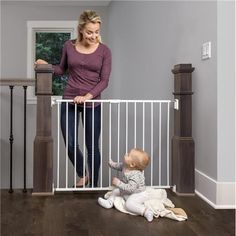 a woman standing next to a baby in a white gate