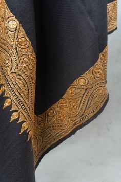 The 'Ebony Twilight Hand-Tilla Embroidered Opulent Shawl' is a masterpiece of traditional opulence, reflecting the serene beauty of the night sky. With its sumptuous black fabric, this shawl becomes a canvas for the radiant Tilla embroidery, which is meticulously applied by hand, honoring the age-old traditions of Kashmiri artisans. The shawl is edged with an intricate golden pattern, reminiscent of the delicate filigree work found in timeless jewelry pieces. This embroidery, with its floral and paisley accents, adds an imperial touch to the shawl, while the scalloped edges of the Tilla work introduce a textural contrast that is both visually appealing and delightful to the touch. This shawl is generously sized, offering warmth and versatility, and can be worn as a luxurious wrap or draped Tilla Work Embroidery, Shawl Embroidery, Tilla Embroidery, Embroidered Rug, Kashmiri Shawls, Golden Pattern, Find Work, Pashmina Shawl, Pashmina Scarf