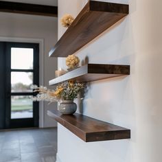 three wooden shelves on the wall with flowers in vases and candle holders next to them