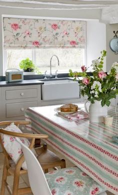 a kitchen table with flowers on it in front of a sink and stove top oven