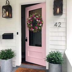 a pink front door with two planters and a wreath