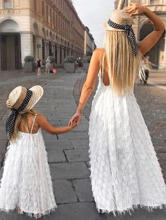 a mother and daughter are walking down the street together, both wearing matching dresses with large hats on their heads