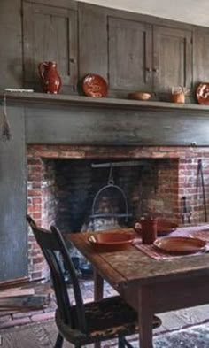 a dining room table with plates and bowls on it, in front of an open fire place