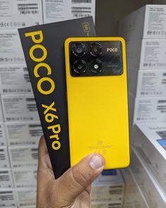 a person holding up a yellow poco x pro phone in front of some boxes