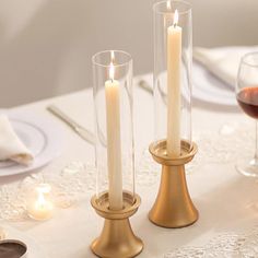 two candles are sitting next to each other on a table with wine glasses and silverware