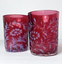 two red glass vases sitting next to each other on a white tableclothed surface