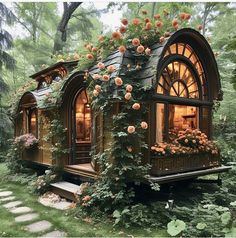 a tiny house with roses growing on the roof and windows, surrounded by greenery