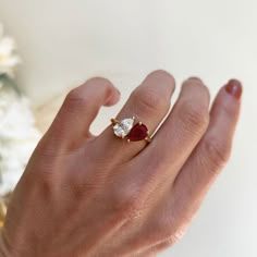 a woman's hand with a diamond and ruby engagement ring on it, next to flowers