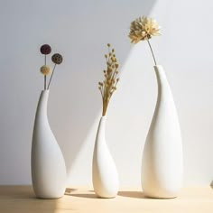 three white vases sitting on top of a wooden table next to each other with flowers in them