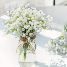 white flowers are in a glass vase on a table with twine and burlap