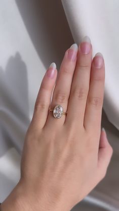 a woman's hand with a diamond ring on her left hand and white silk in the background