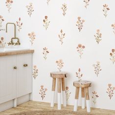 two stools in front of a wall with flowers painted on it and a sink