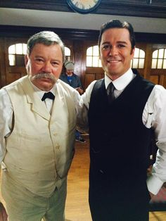 two men standing next to each other in front of a clock